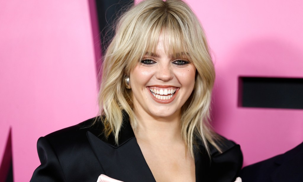 Renee Rapp smililng in front of a pink Mean Girls background.