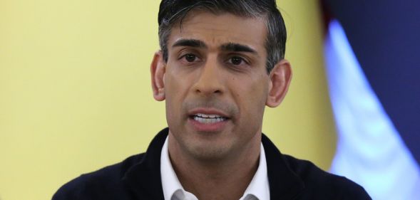 Rishi Sunak, speaking infront of a yellow flag during a news conference.