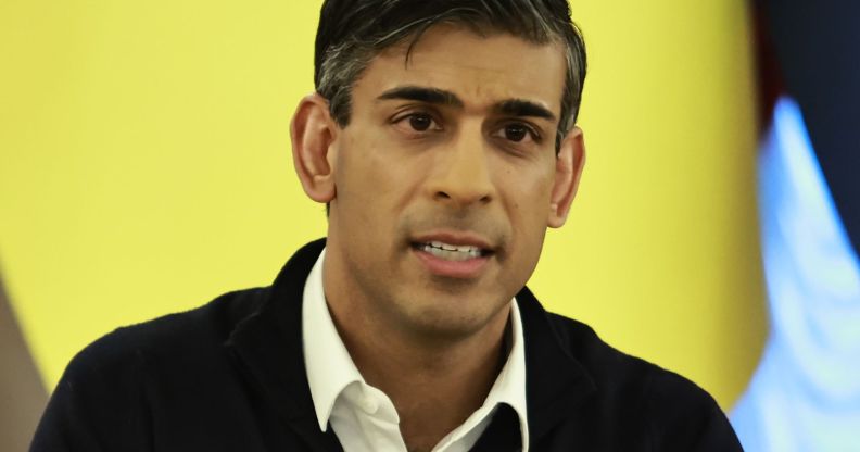 Rishi Sunak, with teeth gritted, infront of a yellow flag.