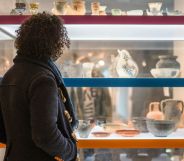 A woman stares and a museum exhibit with rows of ancient clay pots on display.