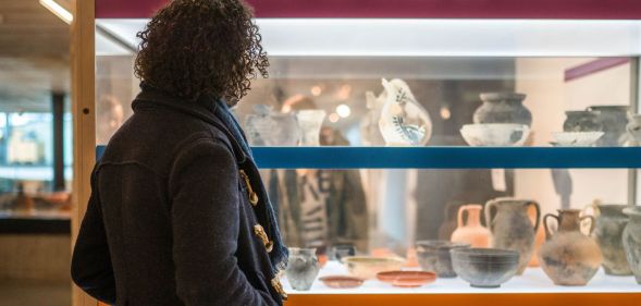 A woman stares and a museum exhibit with rows of ancient clay pots on display.