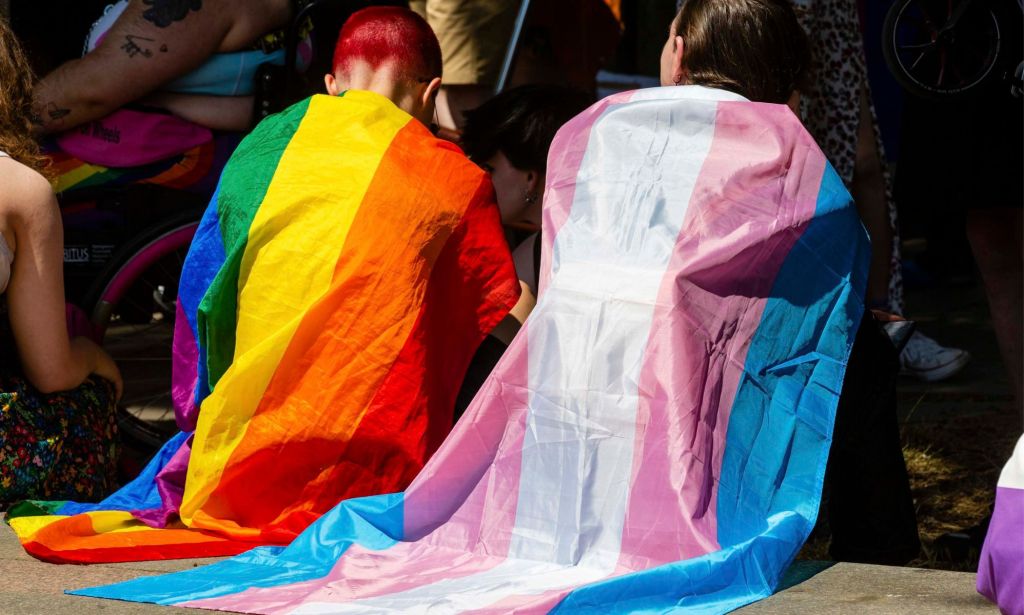 Two activists wearing LGBTQ+ flags at a Pride event.