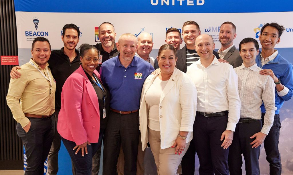 This is an image of a diverse group of people standing in front of a United Airlines sign. 