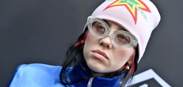 Billie Eilish, who created a song for the Barbie soundtrack, wears a blue jacket, glasses and a pink beanie with a neon star pattern on it