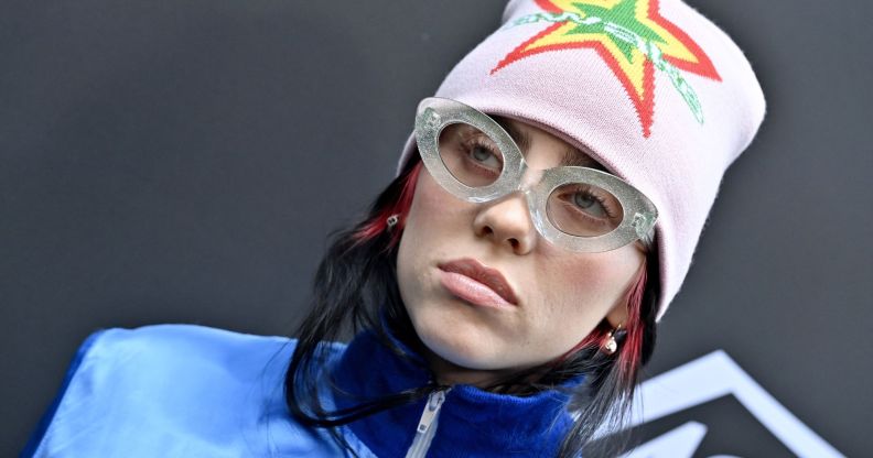 Billie Eilish, who created a song for the Barbie soundtrack, wears a blue jacket, glasses and a pink beanie with a neon star pattern on it