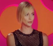 Charlize Theron wears a black outfit as she sits in front of a pink and orange background as a guest judge on Drag Race