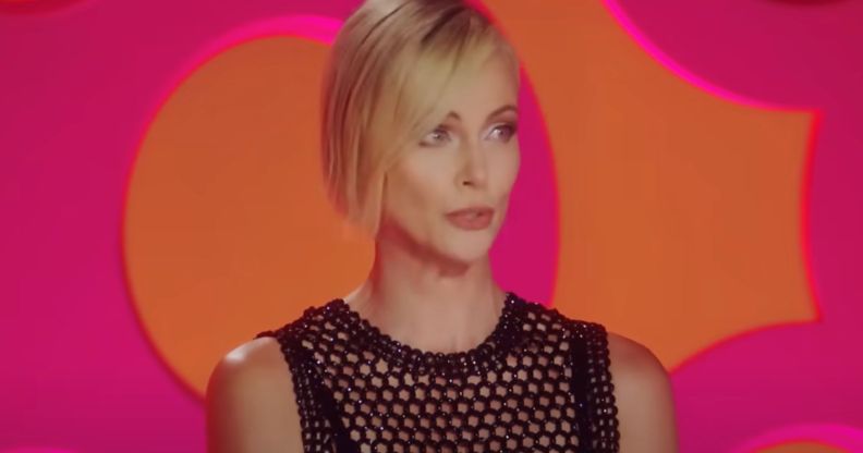 Charlize Theron wears a black outfit as she sits in front of a pink and orange background as a guest judge on Drag Race