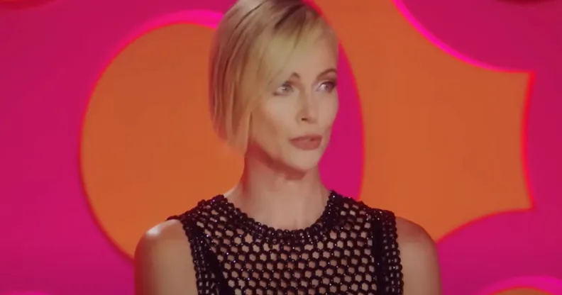 Charlize Theron wears a black outfit as she sits in front of a pink and orange background as a guest judge on Drag Race