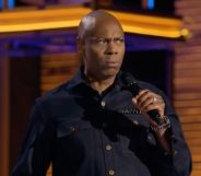 Dave Chappelle, who has faced backlash for making anti-trans jokes, wears a dark shirt as he speaks into a microphone in his new Netflix special The Dreamer