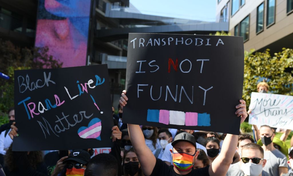 A group of people hold up signs in support of the trans community after Netflix's Ted Sarandos defended Dave Chappelle