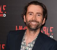 David Tennant, who is set to host the 2024 BAFTAs, smiles while wearing a black and white patterned shirt and dark jacket
