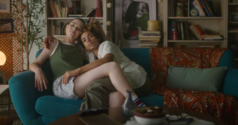 Screenshot of an eHarmony advert shows queer couple sitting together on a sofa hugging