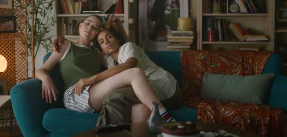 Screenshot of an eHarmony advert shows queer couple sitting together on a sofa hugging