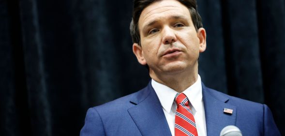 A picture of Florida governor Ron DeSantis, who signed a controversial book ban law, wears a suit and tie as he speaks into a microphone