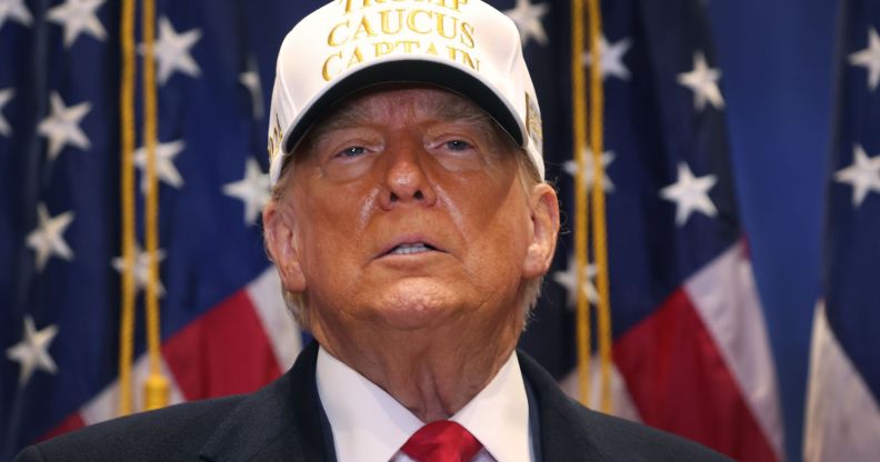 Donald Trump wears a suit and tie with a hat that reads 'Trump caucus captain' at the 2024 Iowa caucus