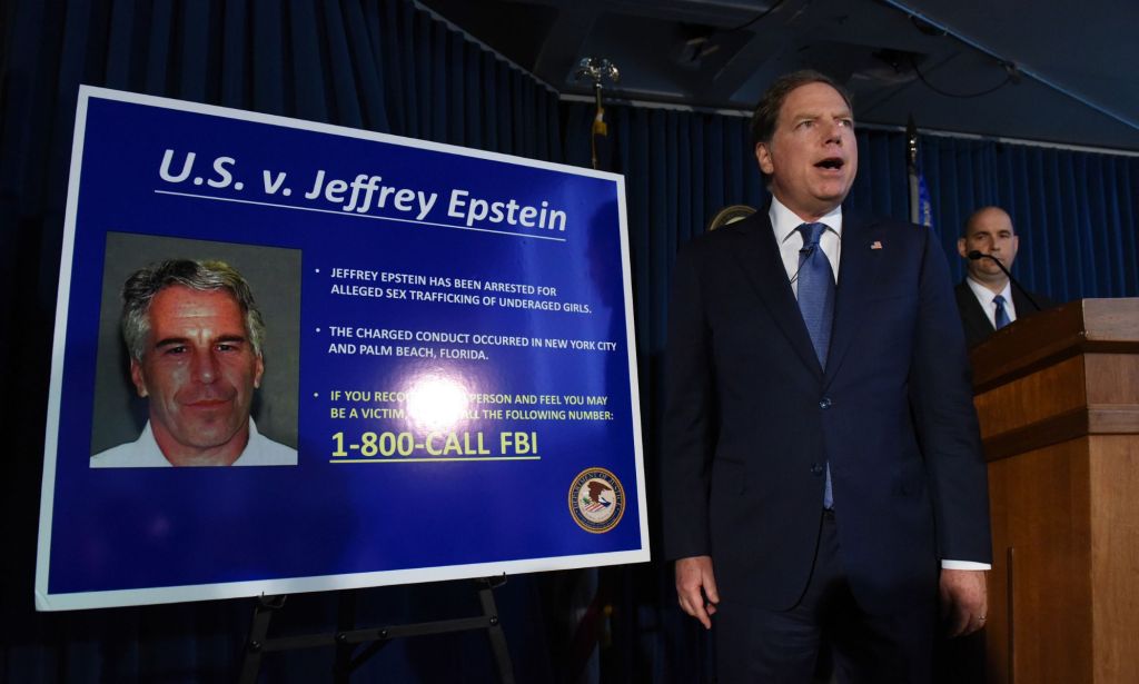 A picture of a lawyer, wearing a suit and tie, standing in front of board detailing the charges against Jeffrey Epstein
