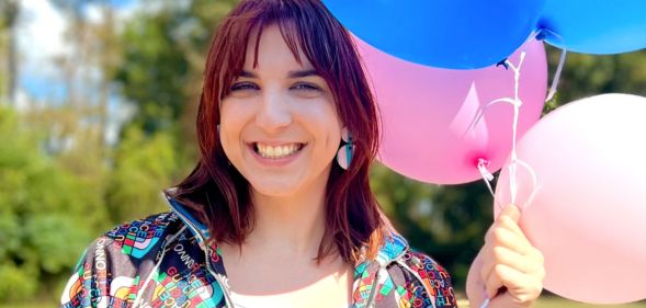 Kris Tyson, a YouTuber and MrBeast collaborator who is trans, smiles as she holds up pink and blue balloons next to her