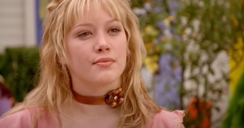 A still of Hilary Duff wearing a pink shirt and copper colour choker with a flower on it as she portrays the Disney Channel character Lizzie McGuire