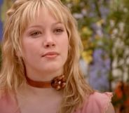 A still of Hilary Duff wearing a pink shirt and copper colour choker with a flower on it as she portrays the Disney Channel character Lizzie McGuire