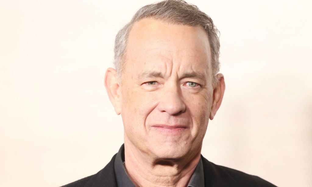Tom Hanks, a non-LGBTQ+ actor who played a queer role previously, looks towards the camera while wearing a dark shirt and dark jacket