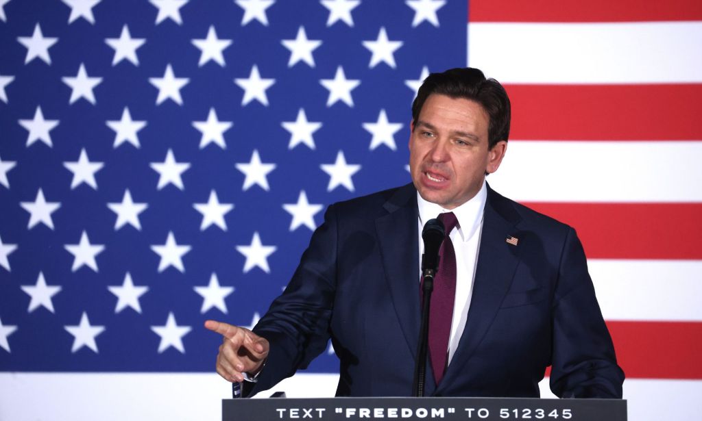 Florida governor Ron DeSantis, who once was a top candidate in the 2024 Republican presidential race, points with one finger as he speaks to supporters in front of a red, white and blue flag