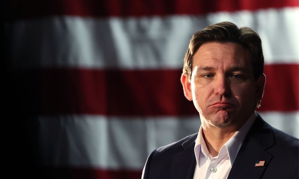 Florida governor Ron DeSantis, who once was a top candidate in the 2024 Republican presidential race, has a forlorn expression on his face as he stands in front of the red and white stripes of the US flag