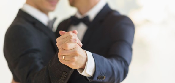 Two grooms clasping hands with a wedding ring visible