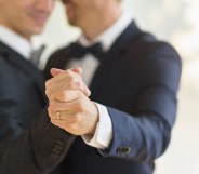Two grooms clasping hands with a wedding ring visible