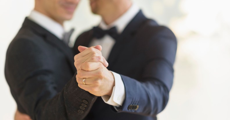 Two grooms clasping hands with a wedding ring visible
