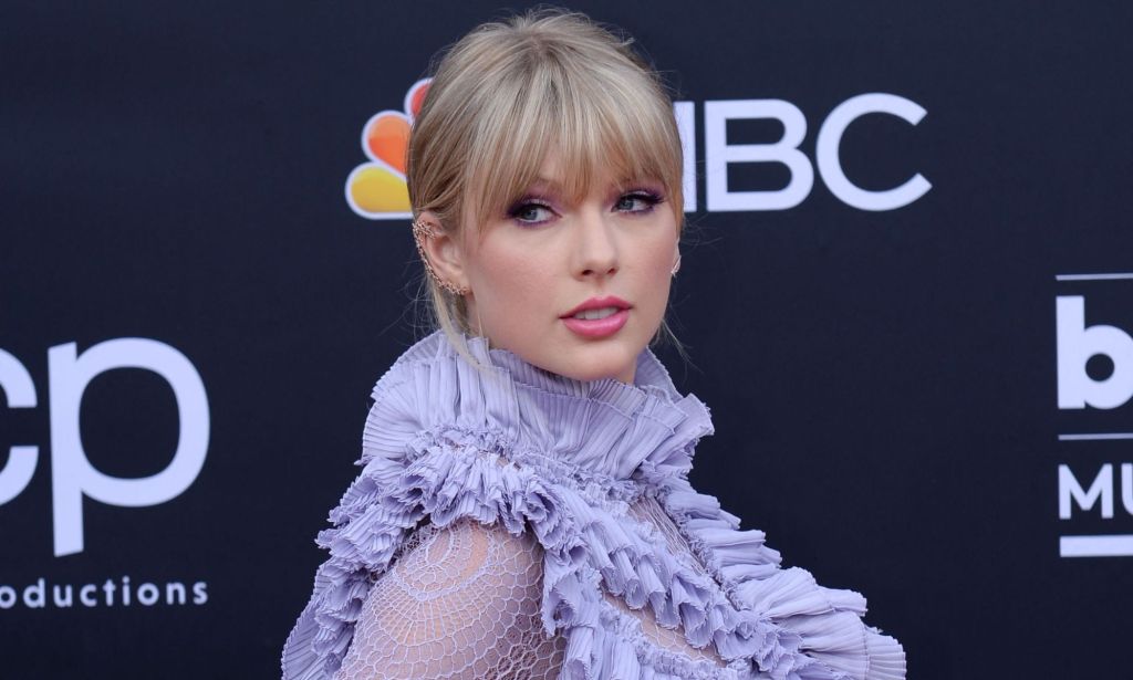 Singer Taylor Swift wears a frilly light purple outfit as she stands in front of a dark blue background