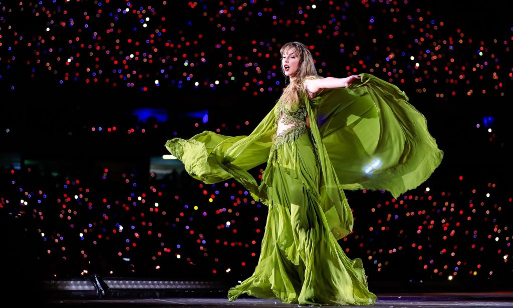 Taylor Swift holds up the pillowing sleeves of a green dress while performing on stage. Her team is reportedly furious after the New York Times published an op-ed that claimed Taylor Swift had been hinting she's queer throughout her career