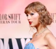 Taylor Swift wears a blue dress while standing in front of a background for her Eras tour. Her team is reportedly furious after the New York Times published an op-ed that claimed Taylor Swift had been hinting she's queer throughout her career