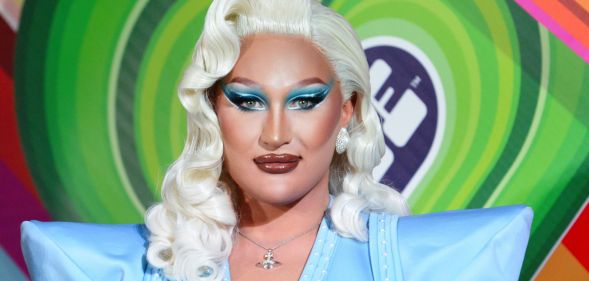 Drag Race Uk star The Vivienne, who is wearing a blonde wig and blue outfit, stares at the camera