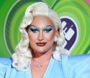 Drag Race Uk star The Vivienne, who is wearing a blonde wig and blue outfit, stares at the camera