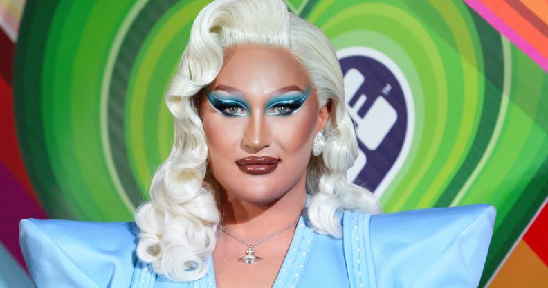 Drag Race Uk star The Vivienne, who is wearing a blonde wig and blue outfit, stares at the camera