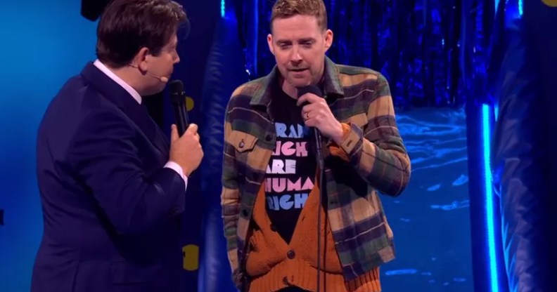 Ricky Wilson pictured on the Michael McIntyre show in a trans rights t-shirt, worn under a plaid shirt