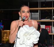 Image shows trans activist Cecilia Gentili at an event, wearing a white dress and holding a microphone