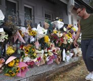 Photo shows a floral display outside Jesse Baird's home with a man walking past in a green short sleeved shirt