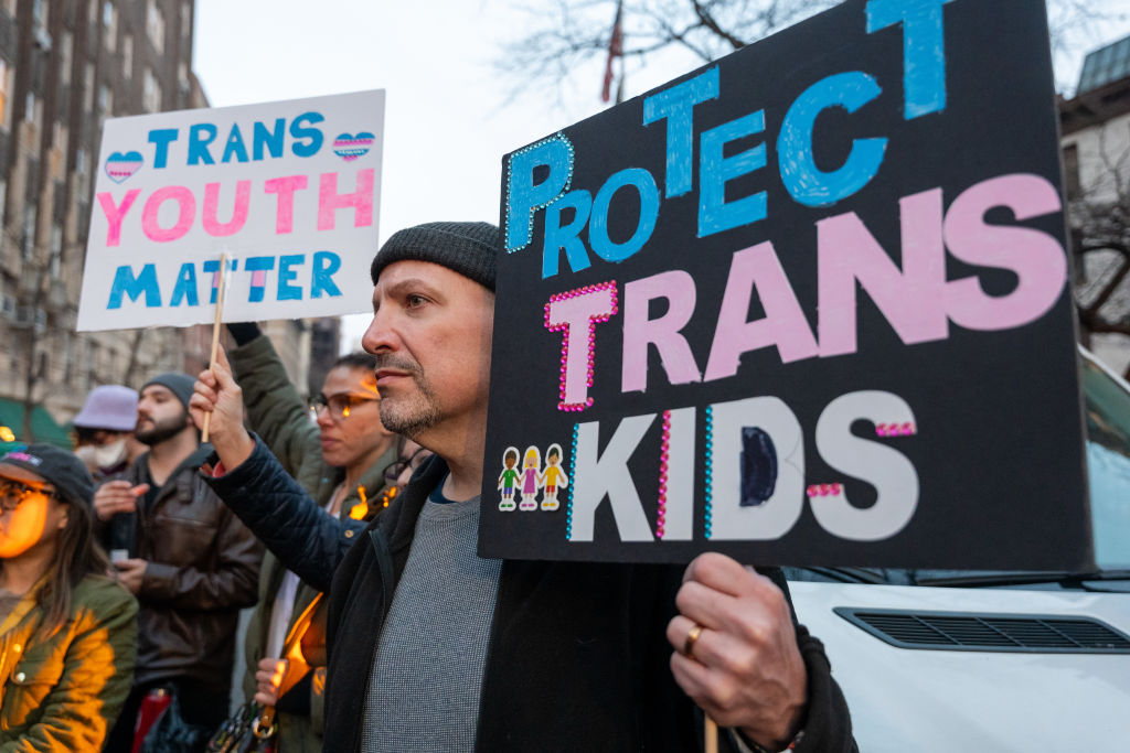 A protester holds a sign saying 'Protect Trans Kids' and 'Trans Youth Matter' at a vigil and protest at the Stonewall Inn