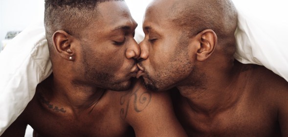 Two Black men in bed kissing under a duvet