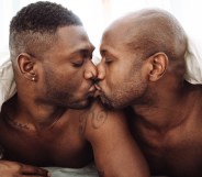 Two Black men in bed kissing under a duvet