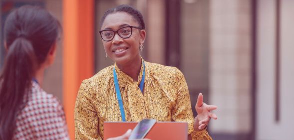 This is an image of a Black woman speaking with a colleague. She is wearing glasses and smiling.