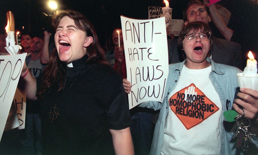 Protestors holding up signs, with one reading "anti-hate laws now" and holding candles dedicated to Matthew Shepard.
