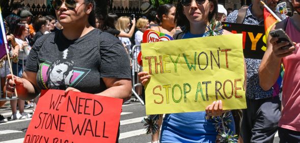 New York City Pride parade with one person holding a sign that says 'We need Stonewall energy right now' and another person holding a sign that says 'They won't stop at Roe'