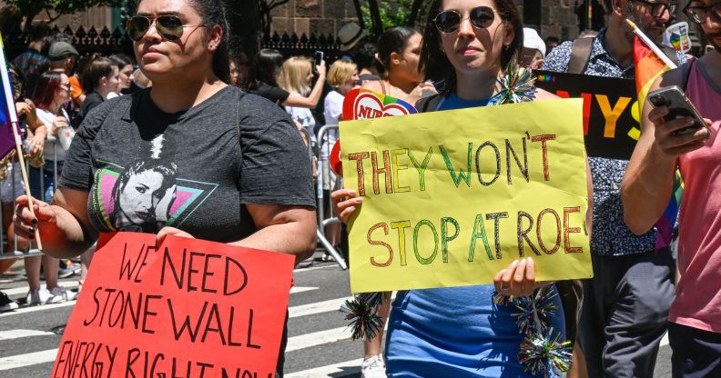 New York City Pride parade with one person holding a sign that says 'We need Stonewall energy right now' and another person holding a sign that says 'They won't stop at Roe'