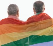 Two elderly people hudle together under a Pride flag.