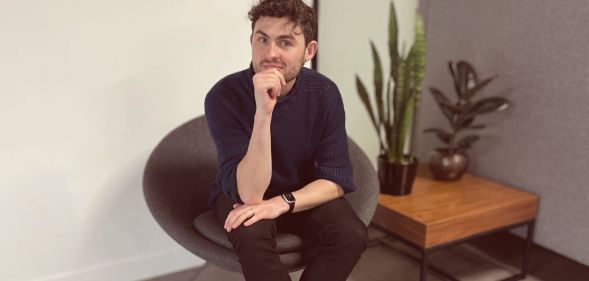 This is an image of a white man sitting in an office. He has on dark clothing