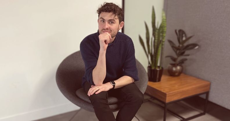 This is an image of a white man sitting in an office. He has on dark clothing