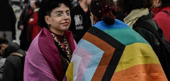Supporters of the LGBTQ community wrapped in LGBTQ+ pride flags gather outside the Greek Parliament.