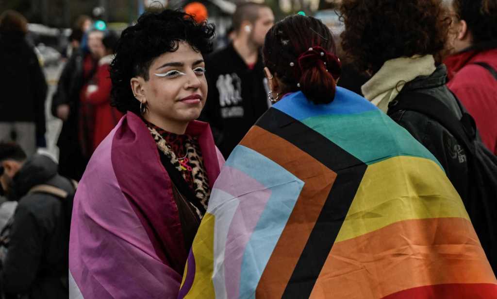 Supporters of the LGBTQ community wrapped in LGBTQ+ pride flags gather outside the Greek Parliament.